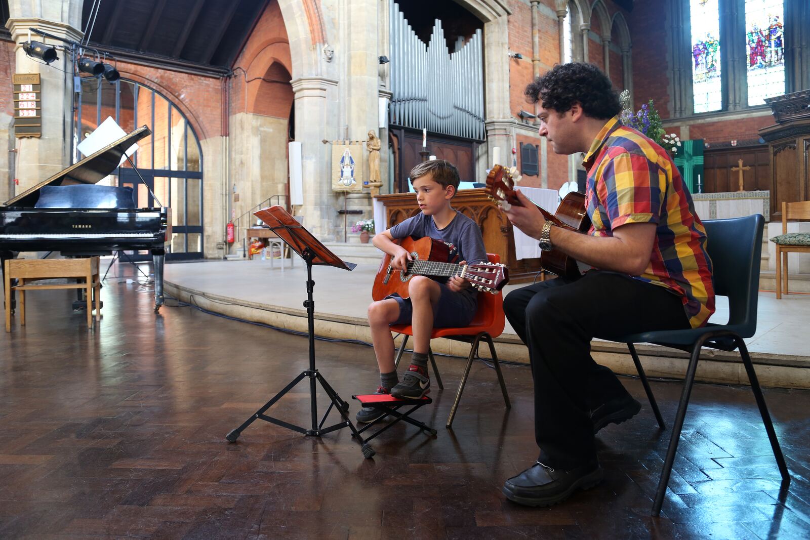 Ben teaching guitar to a young student in a sunlit church hall
