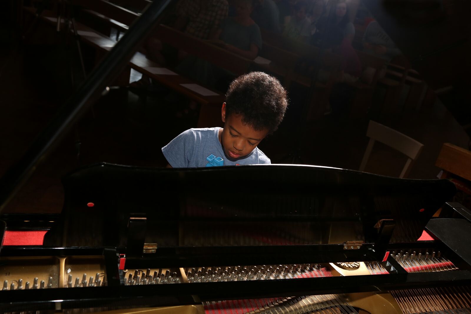 A boy playing a grand piano under a single warm light